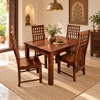 A dark brown wooden dining table with four matching slatted chairs, set on a woven jute rug in a warmly lit, traditional Indian dining room.