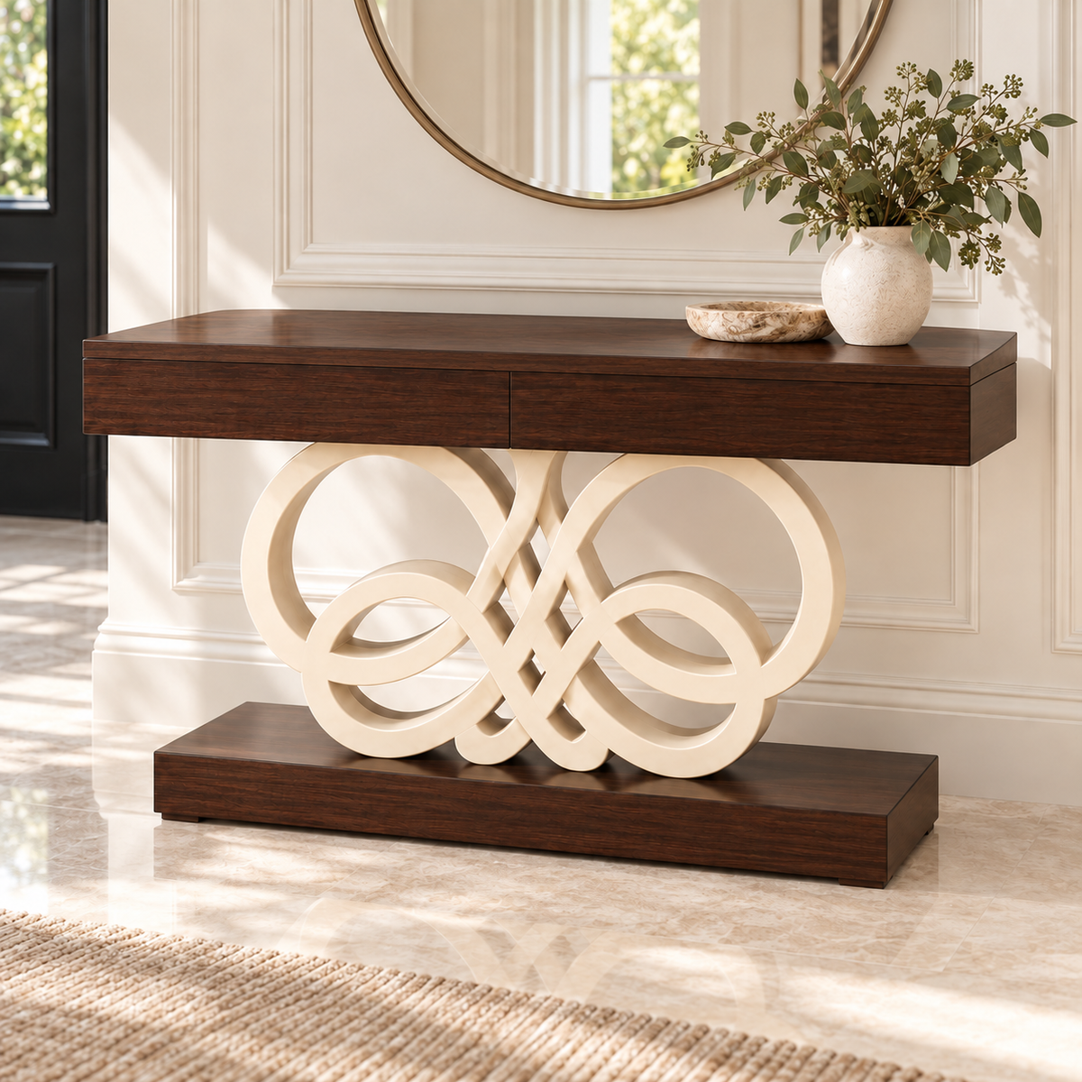 A dark wood console table with a sculptural cream-colored interlocking loop base, styled in a bright entryway with a vase of greenery and a round mirror.